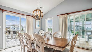 Comedor con mesa y sillas de madera, ventanas grandes con cortinas y un candelabro.