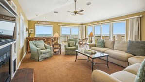 Uma sala de estar espaçosa com lareira, assentos confortáveis e grandes janelas com vista para a praia.