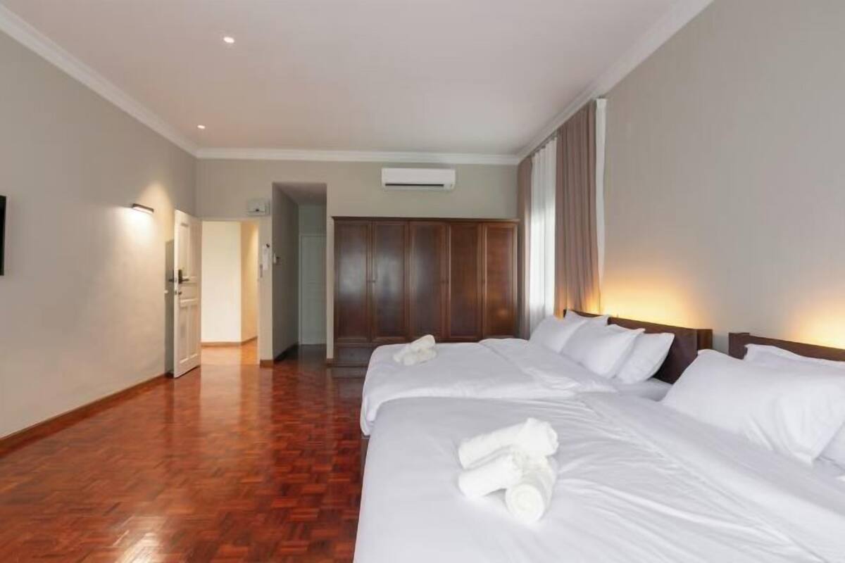 Une chambre d’hôtel avec un plancher en bois, un grand lit avec du linge de lit blanc, une armoire et un appareil de climatisation.