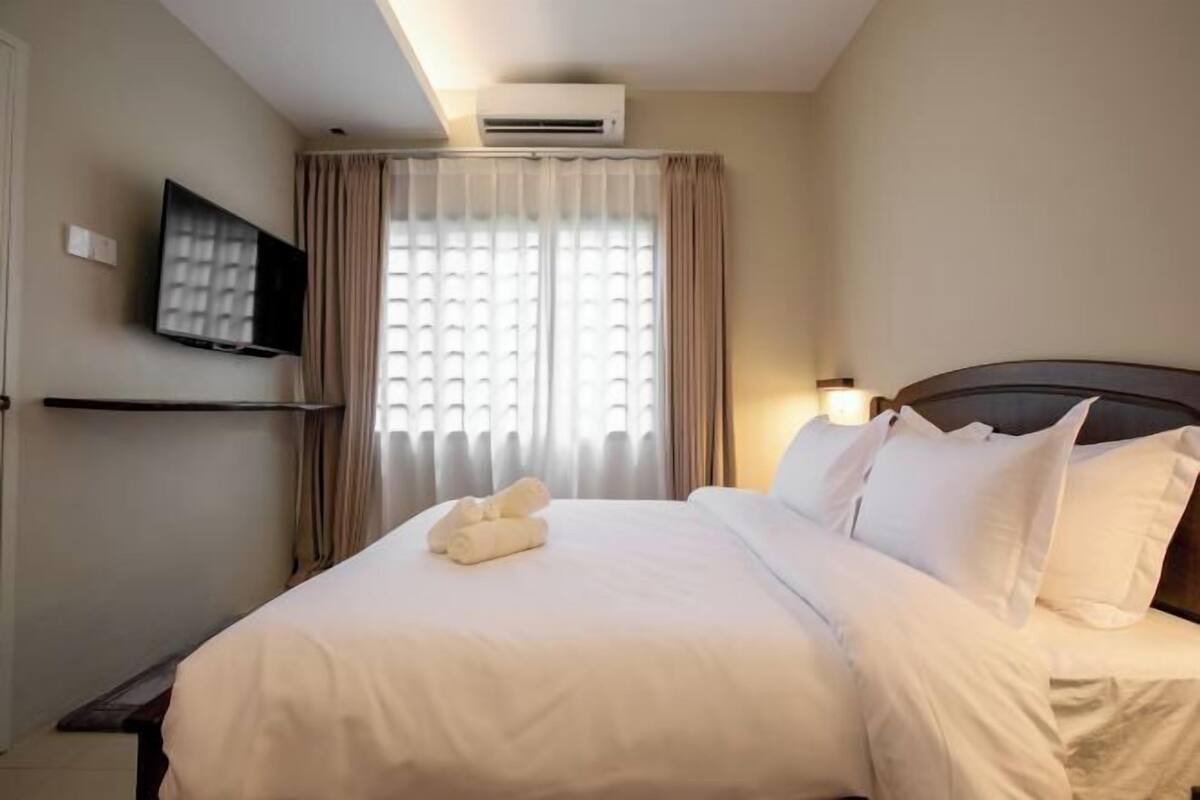 Une chambre d’hôtel équipée d’un lit, d’un téléviseur à écran plat fixé au mur, d’une fenêtre avec des rideaux et d’un appareil de climatisation.