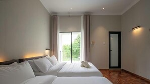 Een hotelkamer met twee bedden, een groot raam met gordijnen, een houten vloer en een deur met een zwarte omlijsting.