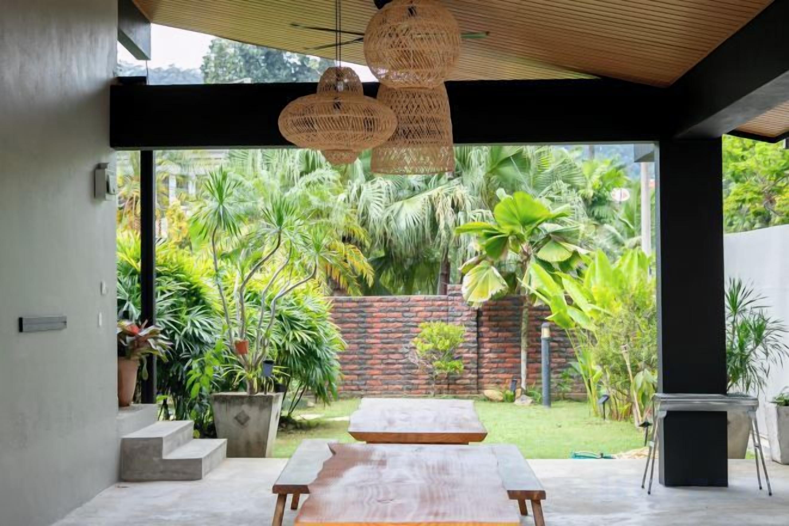 A modern interior with a large table, hanging wicker lights, and a view of a lush garden.