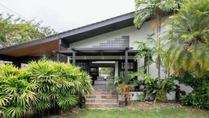 Een modern huis met een overdekte veranda, omringd door weelderige tropische planten.