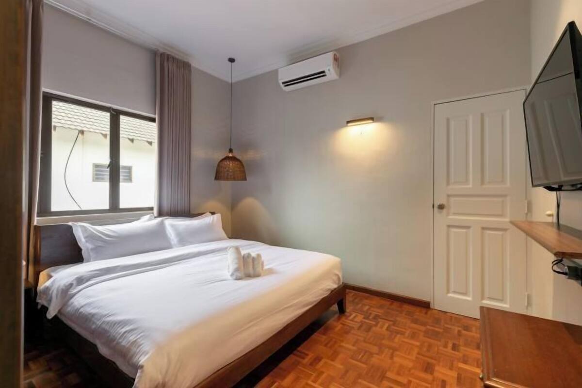 Une chambre d’hôtel avec un lit, une fenêtre, un climatiseur, un téléviseur fixé au mur et un plancher en bois.