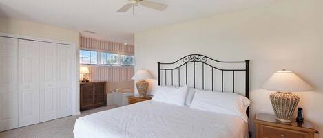 A bedroom with a bed, nightstands, a ceiling fan, a dresser, and a window.