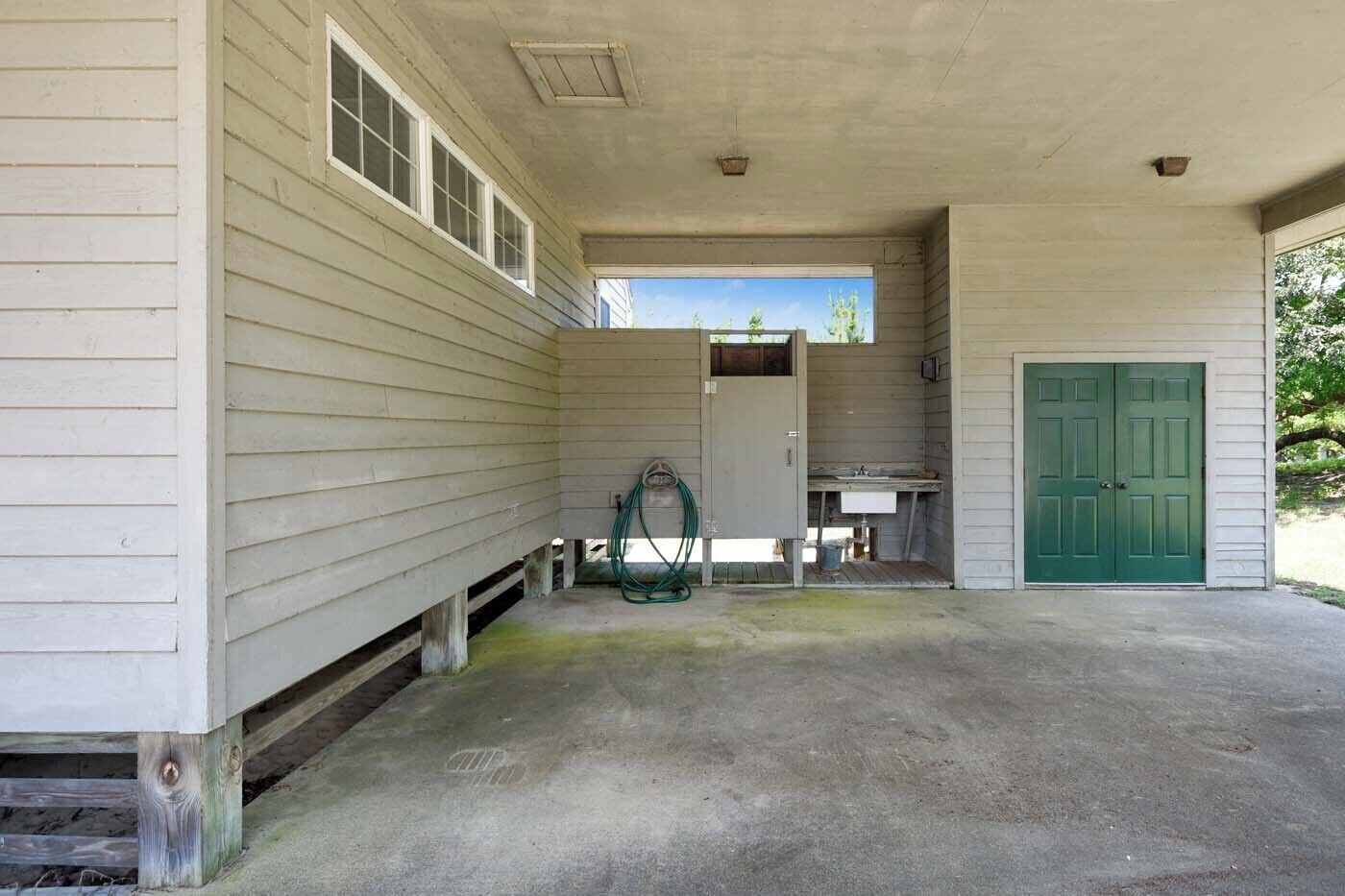 A building with a covered porch, a green door, and a small kitchen area with a sink.