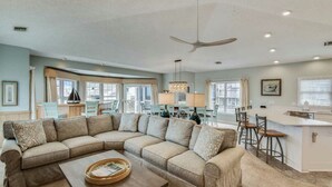 A spacious living room with a large L-shaped sectional sofa, a dining area with a table and chairs, and a kitchen area with a bar. - Tappan, Ships Watch Community in Duck, NC (Duck)