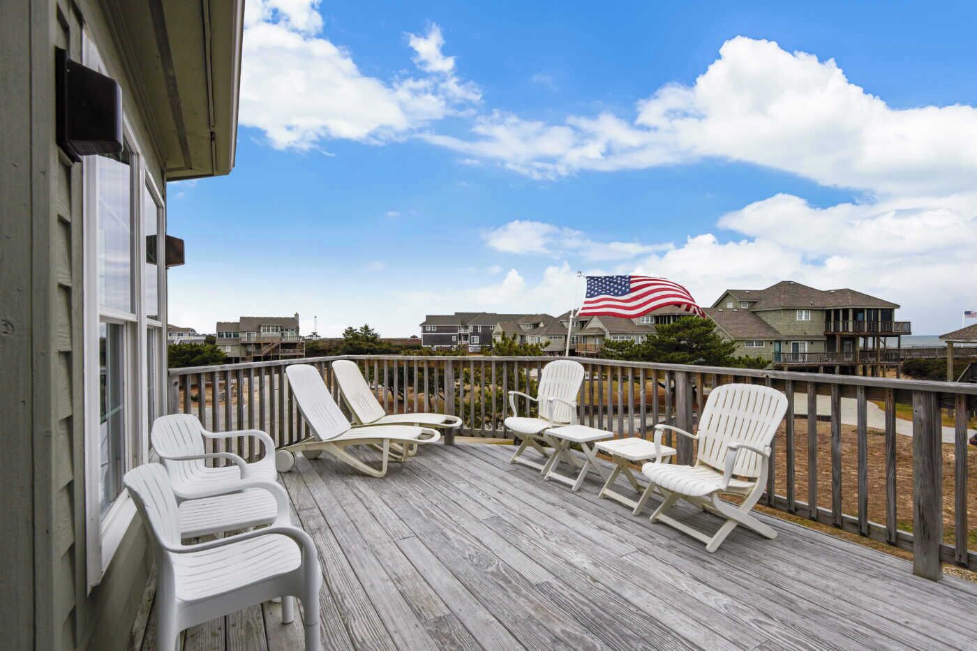 A wooden deck with white chairs and an American flag.
