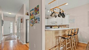 Une cuisine moderne avec des tabourets de bar en bois, un porte-casseroles suspendu et diverses œuvres d’art accrochées aux murs.
