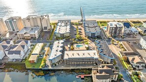 An aerial view of a coastal urban area with modern buildings, a pier, and a swimming pool.