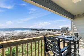 A balcony with a view of the beach and pier, wooden furniture, and a clear sky. - Sea Cabin 120- Oceanfront 1BR/1BA- Pool (North Myrtle Beach)