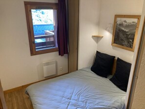 A bedroom with a bed, a window with curtains, a radiator, and a framed picture on the wall.