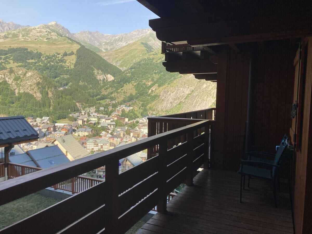 A wooden balcony with a view of a town and mountains.