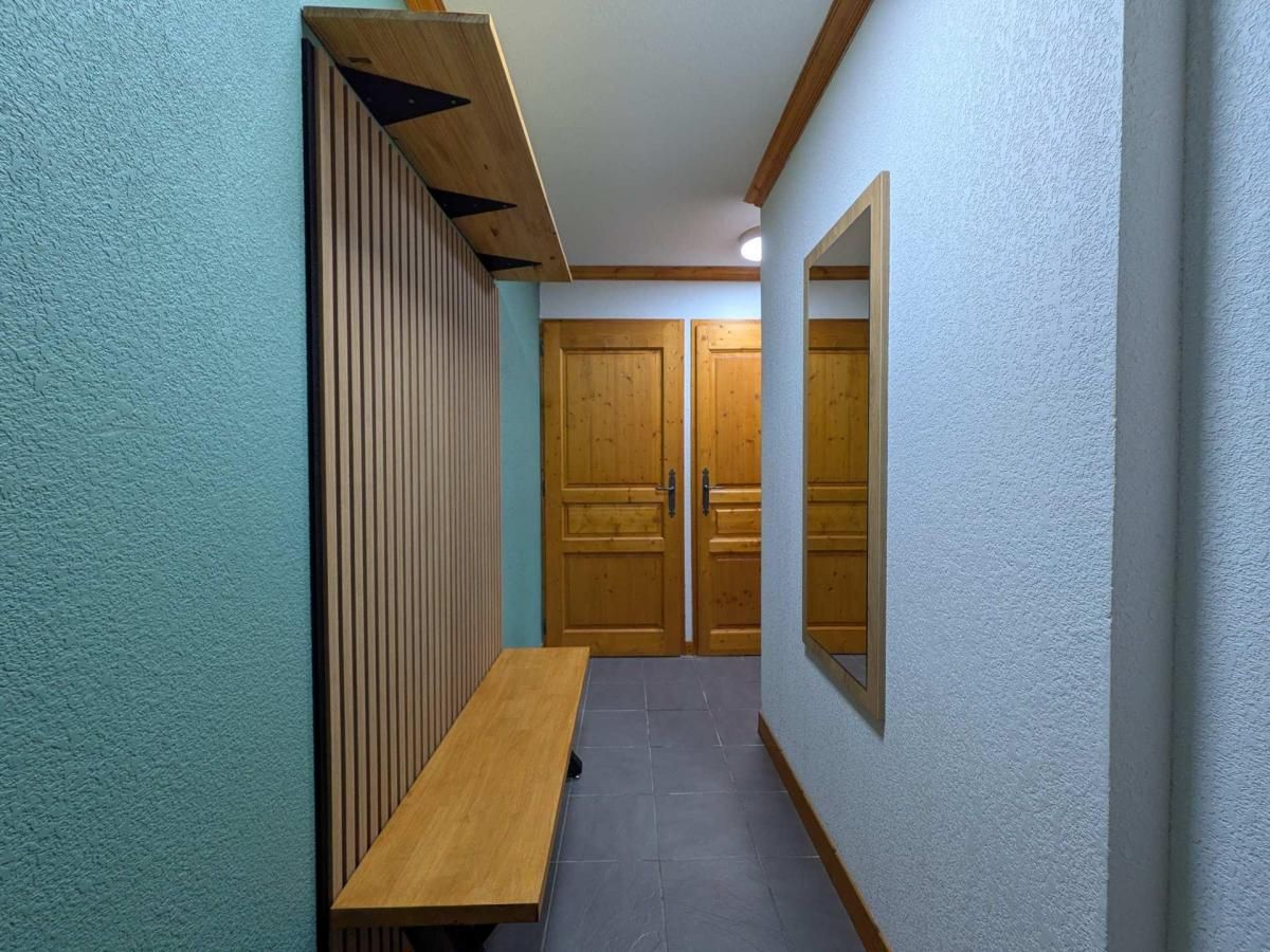 A hallway with a wooden bench, two wooden doors, and a wall-mounted mirror.