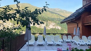 Terraço com espreguiçadeiras e guarda-sóis, com vista para uma paisagem montanhosa.