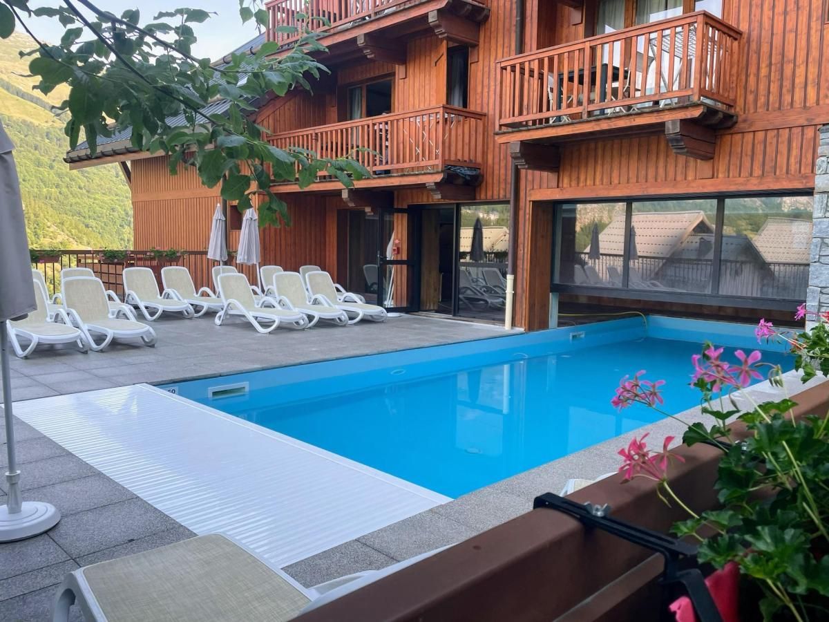 A swimming pool with lounge chairs and a wooden building with balconies.