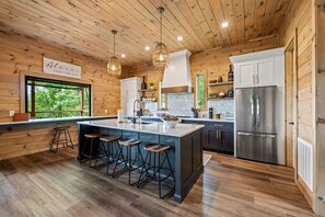 Una cocina moderna con paredes de madera, una isla grande con taburetes de bar, electrodomésticos de acero inoxidable y vistas al exterior.