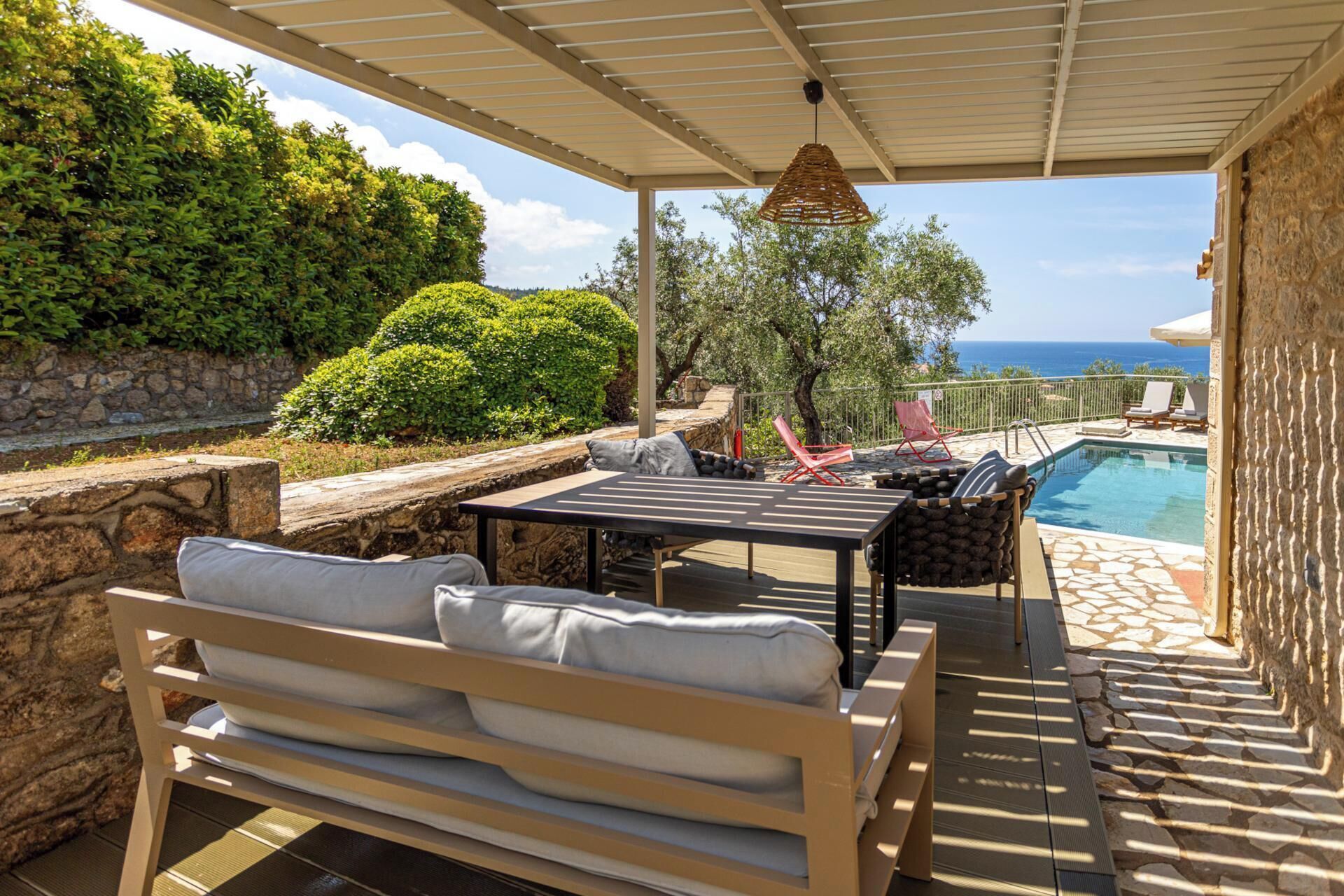 A covered outdoor area with a pool, seating, and a view of the sea.