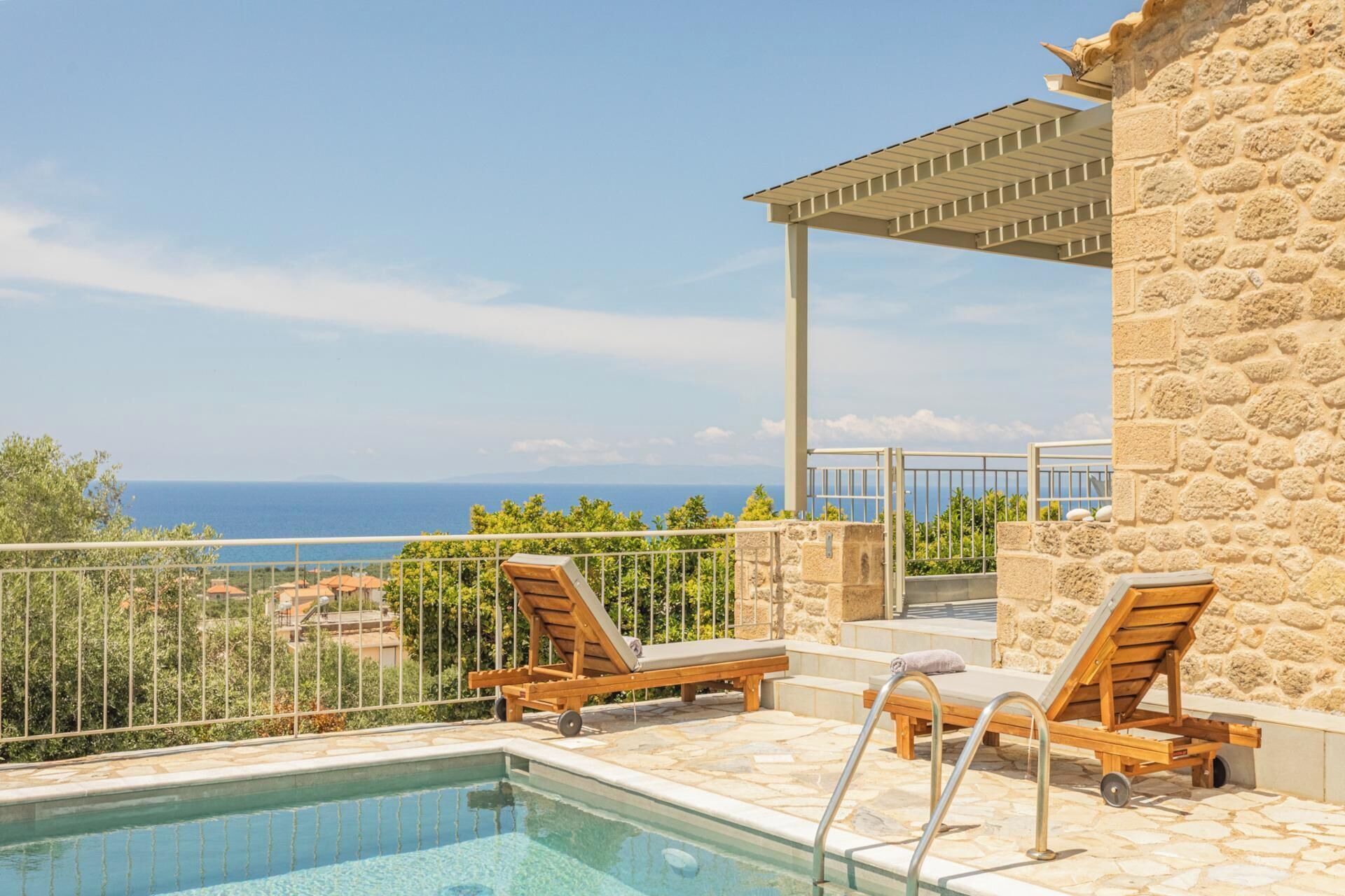 A pool area with lounge chairs and a stone building, overlooking a coastal view.