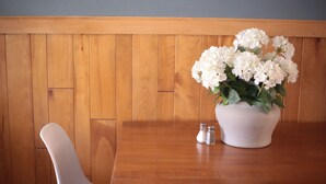 A wooden dining table with a white vase of white flowers and salt and pepper shakers.