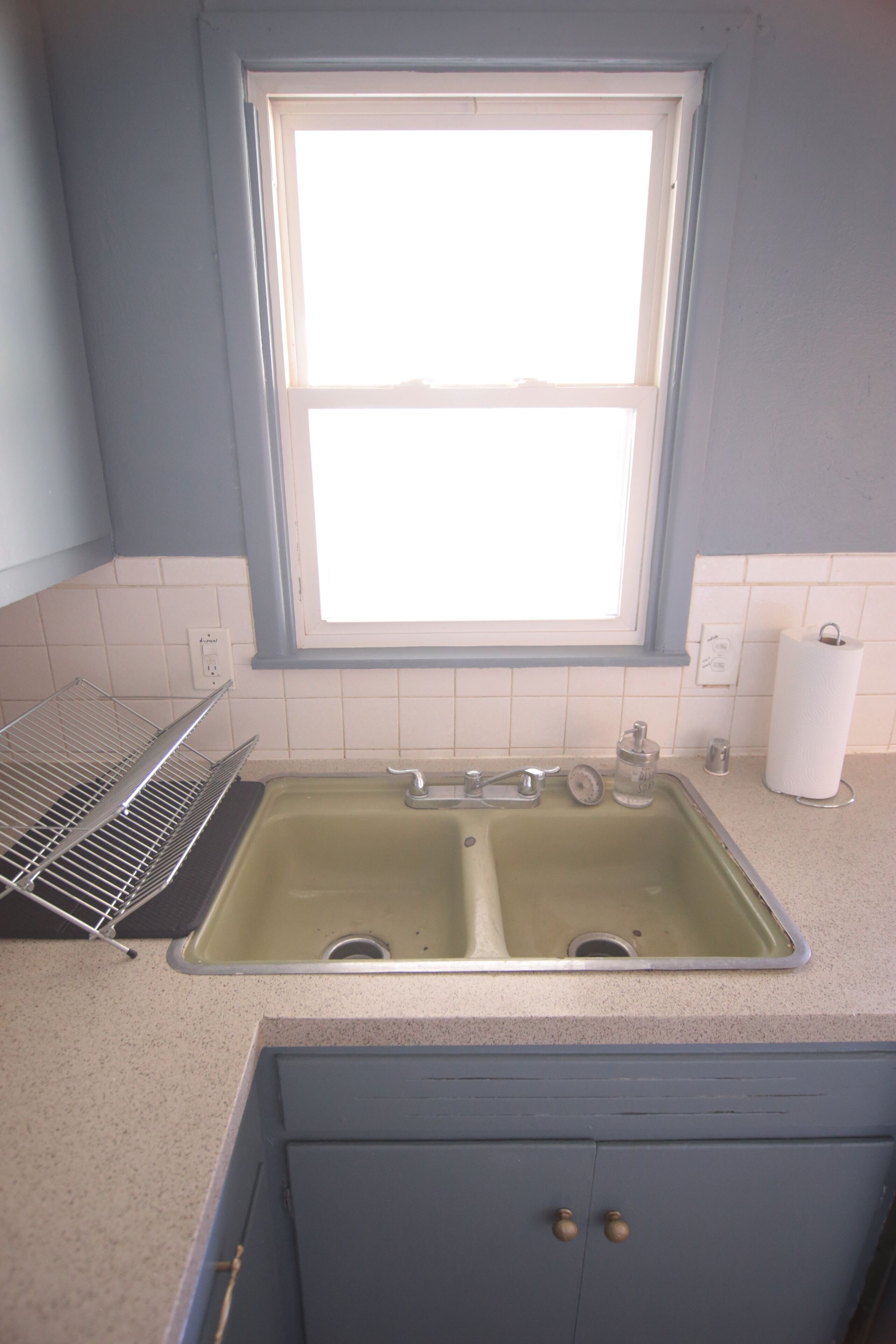 A kitchen with a double sink, a window above the sink, and a countertop with a paper towel holder.