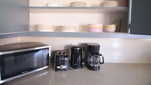 A kitchen with a microwave, toaster, and coffee maker on the counter, and shelves above holding plates and bowls.