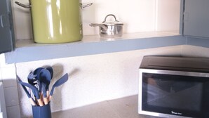 A kitchen with a microwave, a green pot, a colander, and a utensil holder.