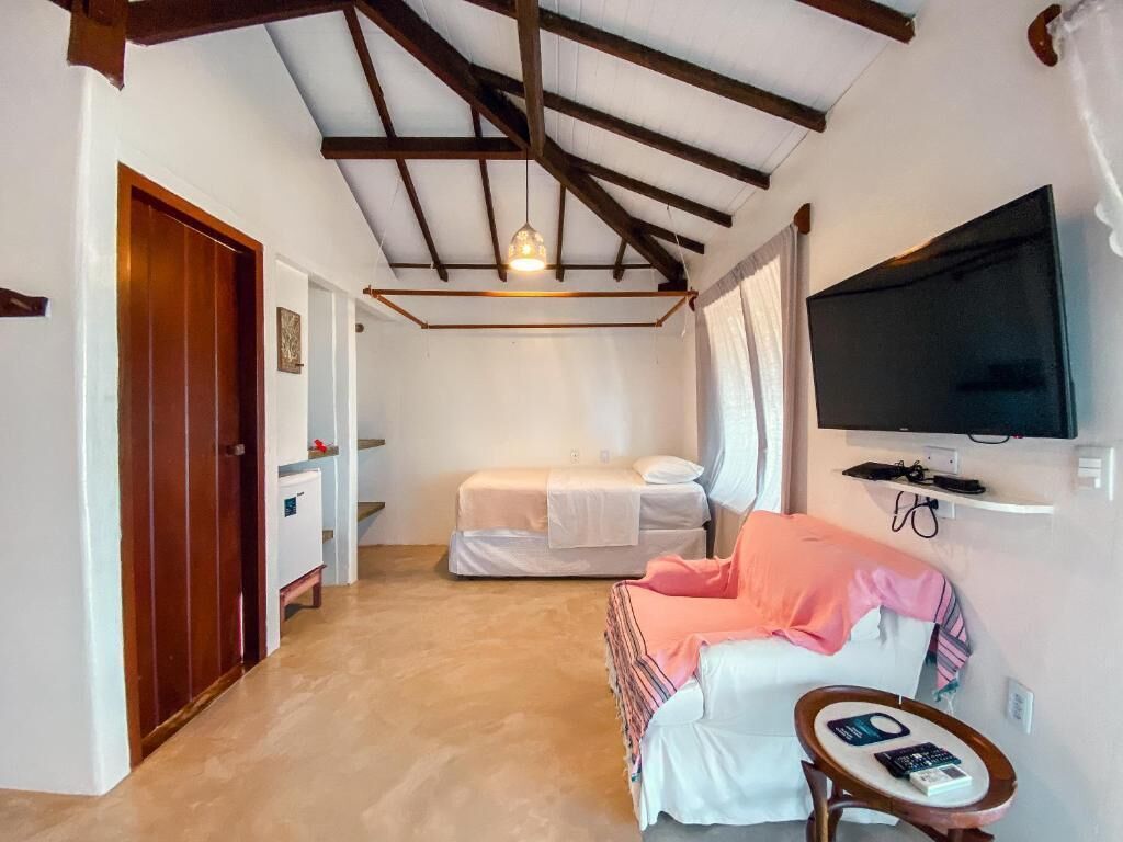 Una habitación con una cama, un televisor montado en la pared, una mesita y una puerta que da a otra habitación.