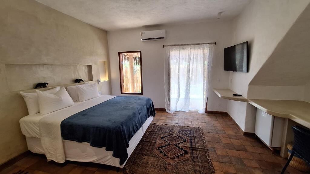 Un dormitorio con cama, televisión, escritorio, ventana con cortinas y una alfombra estampada.
