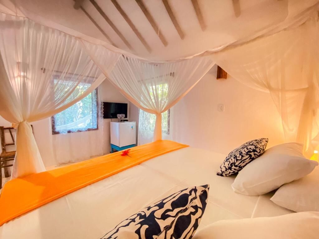 Una cama con ropa de cama blanca y dosel, una mesita de noche de madera y almohadones estampados.