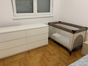 Una habitación con un armario blanco, un corralito para bebé y una ventana con persianas.