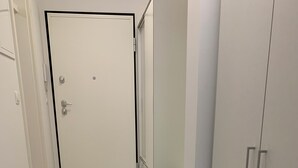 Un pasillo estrecho con una puerta blanca al final, suelo de baldosas y un armario con cajones a la derecha.