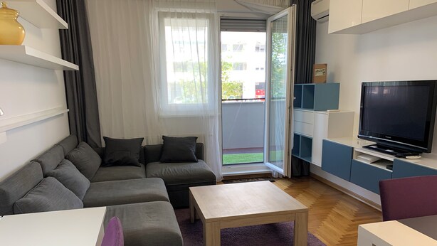Una sala moderna con un sofá gris, una mesa de centro de madera y un televisor sobre un mueble.