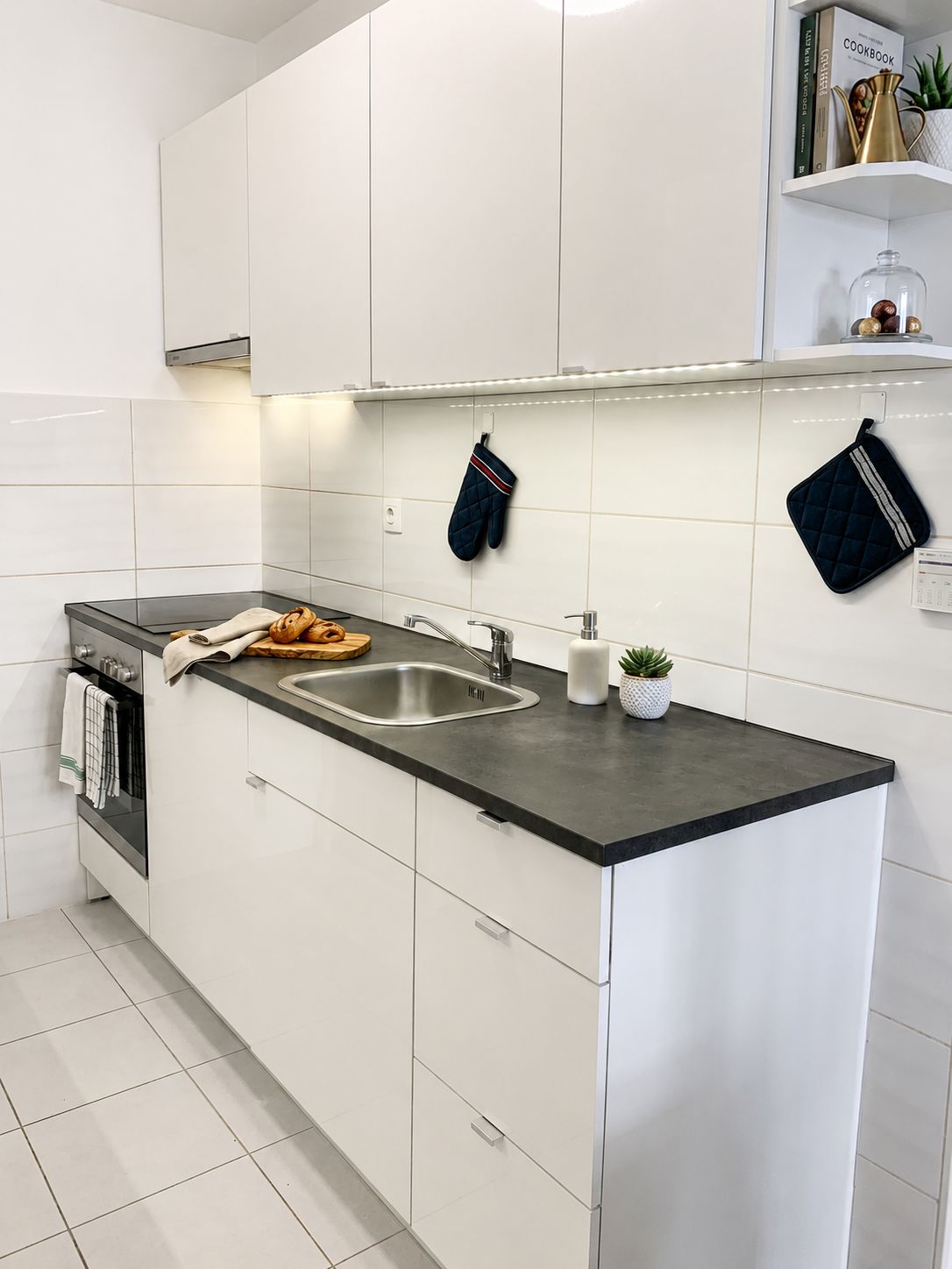 A modern kitchen with white cabinetry, a black countertop, a stainless steel sink, and a small potted plant.