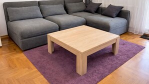 Un sofá gris con varios cojines, una mesa de centro de madera y una alfombra morada sobre un suelo de madera.