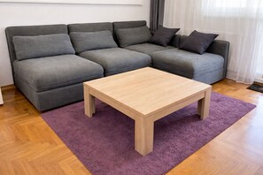 Un sofá gris con varios cojines, una mesa de centro de madera y una alfombra morada sobre un suelo de madera.