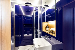Ein modernes Badezimmer mit einer gläsernen Duschkabine, einem weißen Waschbecken und einem Ablagebereich für Toilettenartikel.