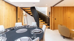 Ein moderner Essbereich mit einem schwarzen Tisch, gedeckt für sechs Personen, einer Wendeltreppe und Holzvertäfelung.