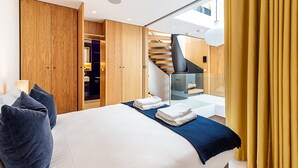 Ein modernes Hotelzimmer mit einem großen Bett, einem Holzschrank, einer Glaskonstruktion als Treppe und Blick zum Himmel.