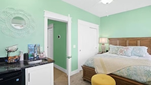 A bedroom with a bed, a nightstand, a lamp, a ceiling fan, and a door leading to another room. - Ocean View Oasis for 8-Food Trucks @ Your Doorstep (Mexico Beach)