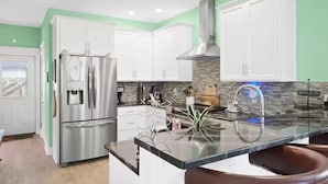 A modern kitchen with white cabinets, stainless steel appliances, and a large island with a sink. - Ocean View Oasis for 8-Food Trucks @ Your Doorstep (Mexico Beach)
