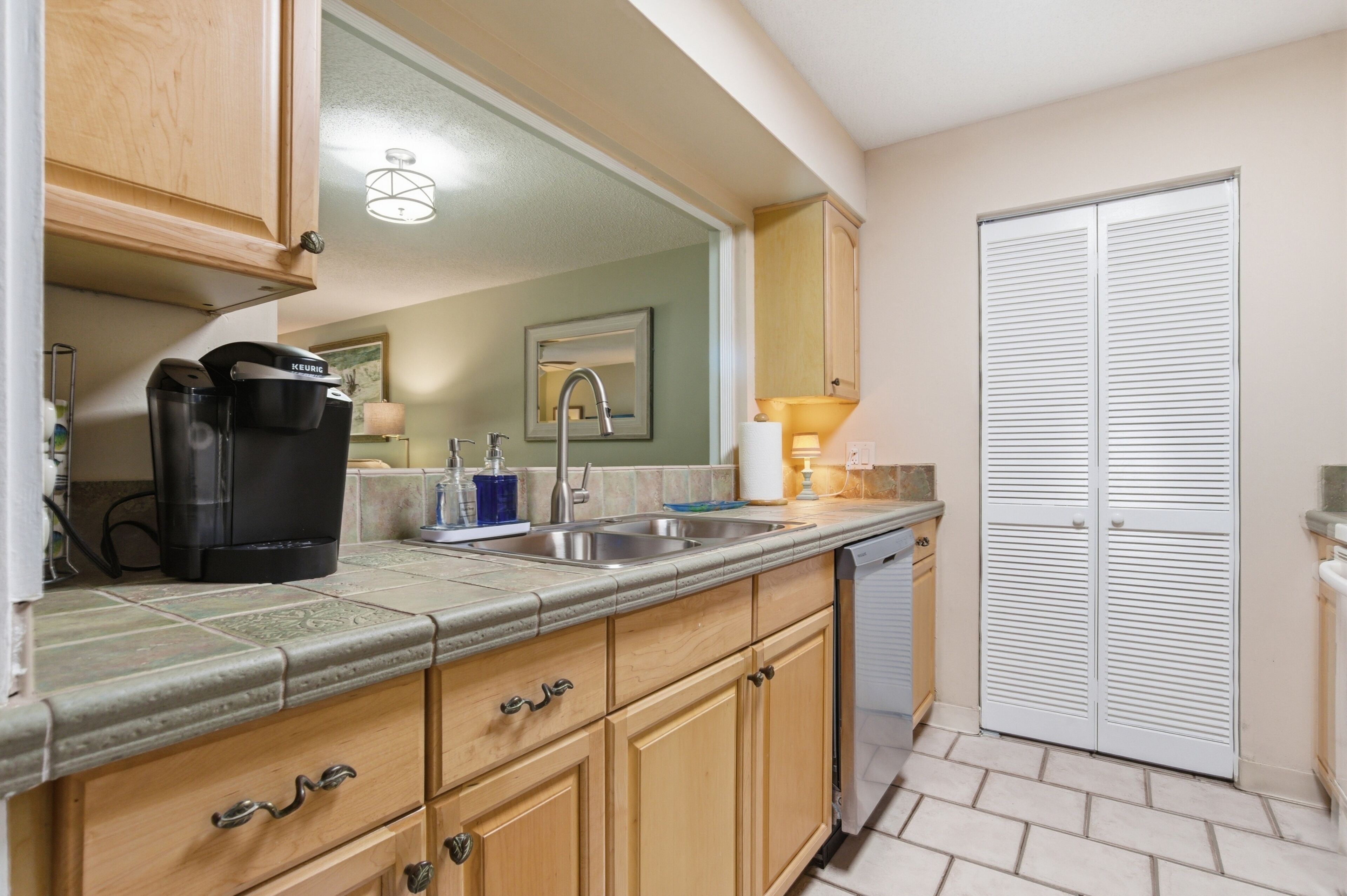 A kitchen with wooden cabinets, a coffee maker, a sink, and a white door.