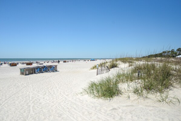 A sandy beach with a bicycle rack, a wooden structure, and sparse vegetation.