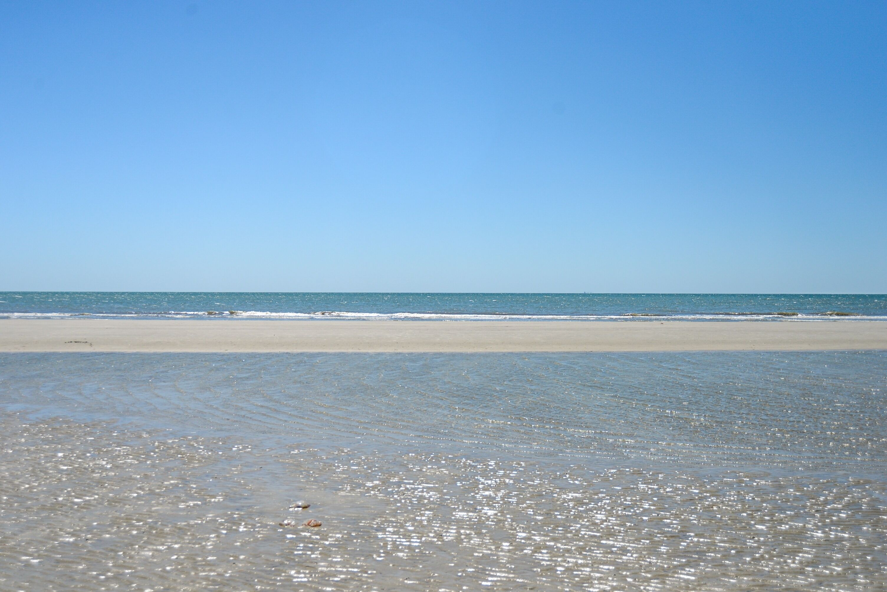 Een strand met heldere lucht en rustig water.