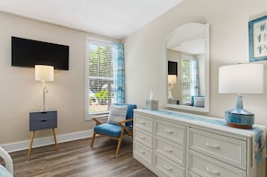 A bedroom with a bed, a dresser, a chair, a TV, and a window with blinds.