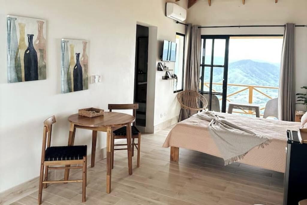 Ein Schlafzimmer mit einem Bett, einem Holztisch, zwei Stühlen und einem Fenster mit Blick auf die Berge.