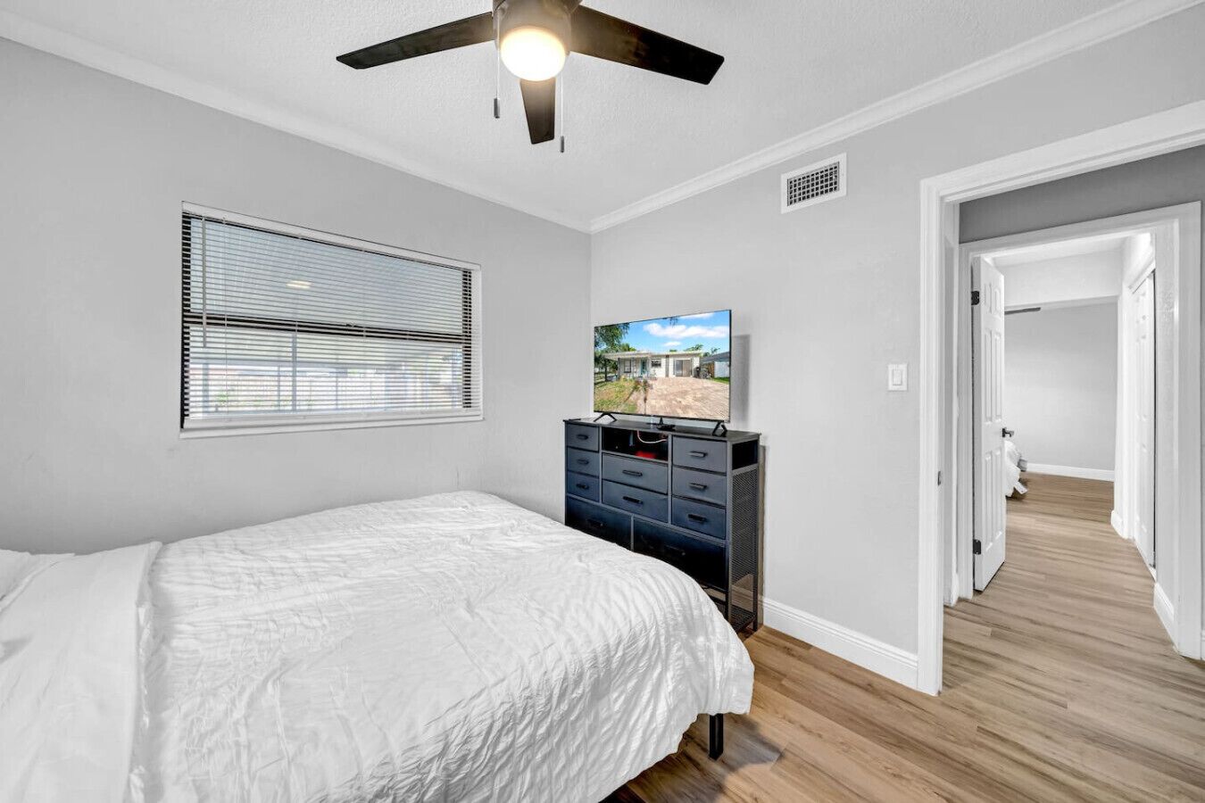 Un dormitorio con cama, cómoda, ventilador de techo, ventana con persianas y televisor sobre una cómoda.