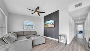 A modern living room with a sectional sofa, a ceiling fan, a flat-screen TV, and a view of the outdoors. - Modern Retreat | Under 15min/Downtown Orlando (Orlando)