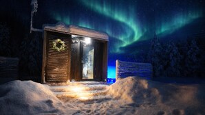 Un edificio cubierto de nieve con un adorno navideño en la puerta, un cartel con el número 24 y vistas de las auroras boreales.