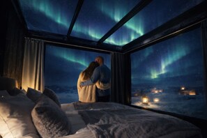 Een kamer met een bed, een raam en uitzicht op het noorderlicht.